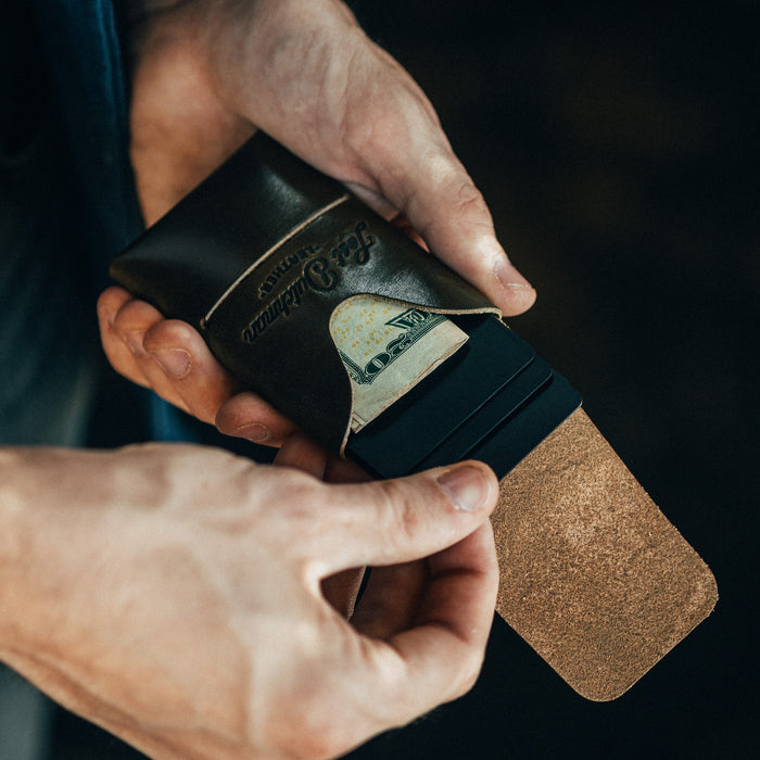 Person holding a leather wallet with money sticking out, against a dark background