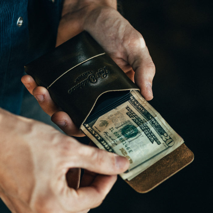 Person holding a leather wallet with money inside against a dark background