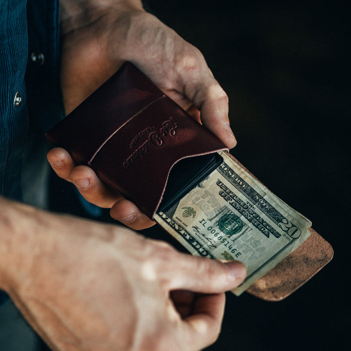 Person holding a leather wallet with a $20 bill inside against a dark background