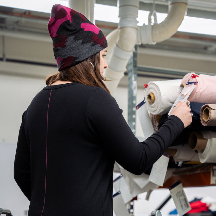 Person in a black long-sleeve shirt and colorful beanie working with rolls of fabric in an industrial setting.