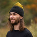 Man wearing a black beanie with yellow pattern and a black shirt outdoors