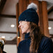 Person wearing a dark blue knit hat with a pom-pom indoors
