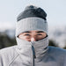 Person wearing a gray winter coat and two beanies in a snowy landscape