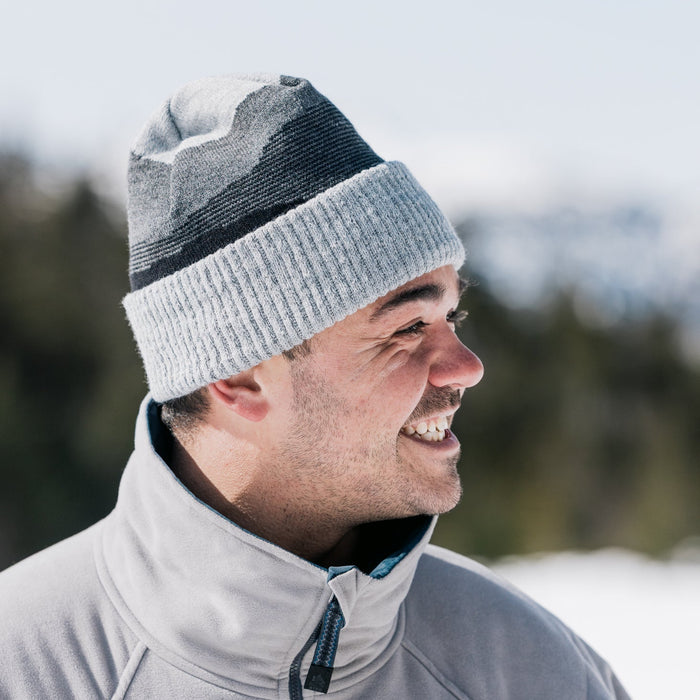 Man wearing a gray knit beanie and light gray jacket outdoors with a blurred natural background