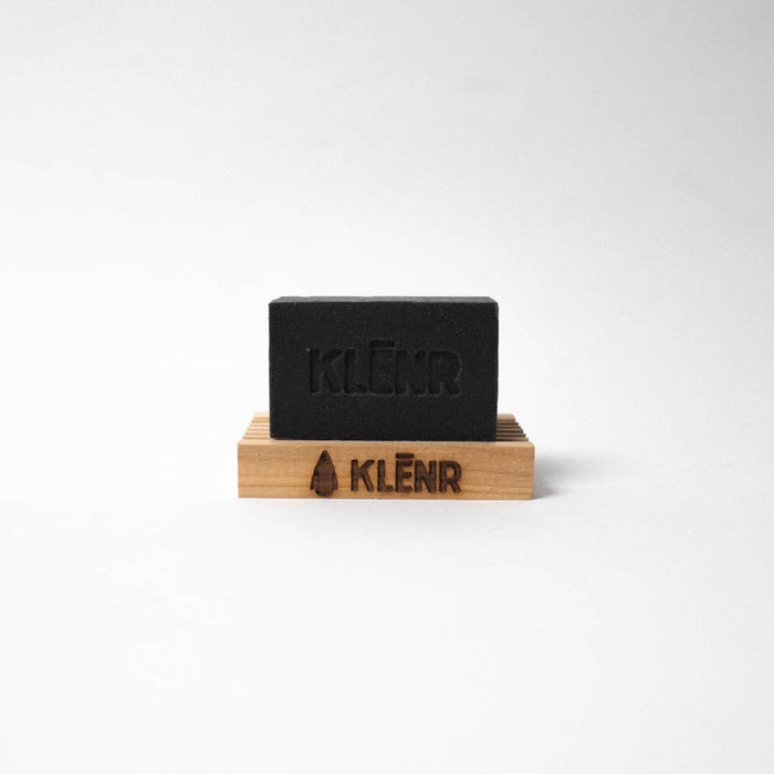 Black bar of soap on a wooden stand with 'KLENR' branding on a white background