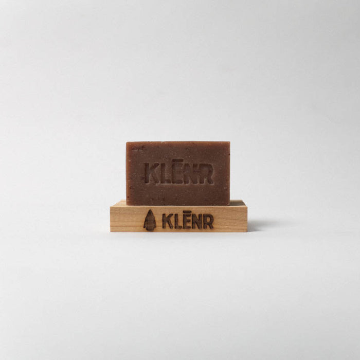 Brown bar of soap on a wooden stand with 'KLENR' branding on a light gray background
