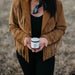 Person wearing a cowboy hat and brown jacket holding a jar in a field