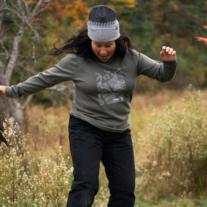 Person in outdoor setting wearing a green sweatshirt with a graphic design, black pants, and brown boots.