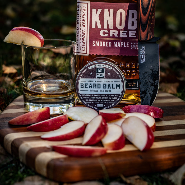 Knob Creek Smoked Maple bourbon bottle with a glass of whiskey, apples, and a knife on a wooden cutting board.