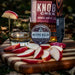 Knob Creek Smoked Maple bourbon bottle with a glass of whiskey, apples, and a knife on a wooden cutting board.