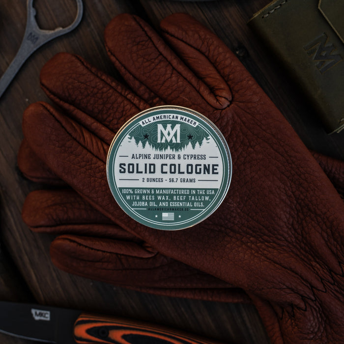Solid cologne container on a pair of brown gloves with a dark background