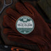 Solid cologne container on a pair of brown gloves with a dark background