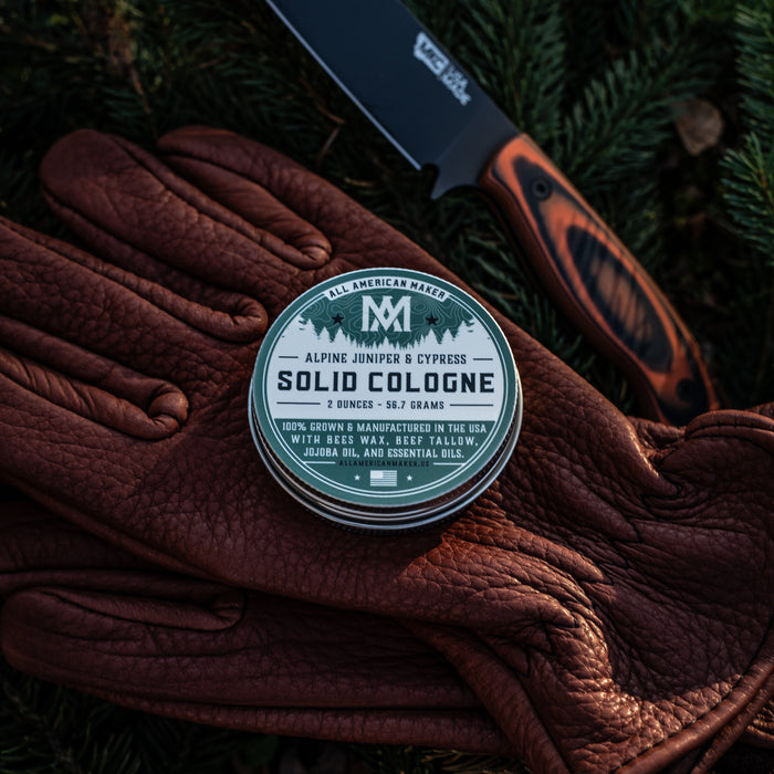 Solid cologne container on brown leather gloves with a knife in the background