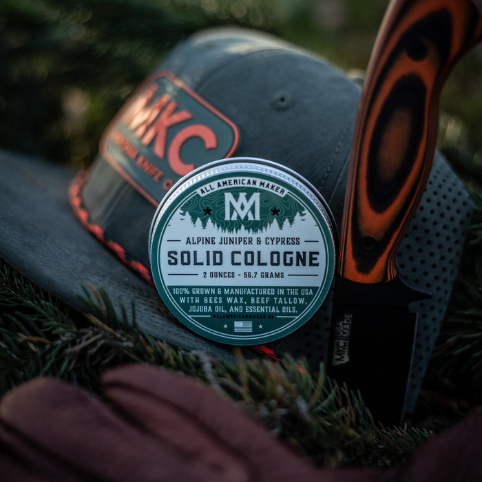 Cap with a cologne bottle labeled 'MJC' and a knife on a grassy background
