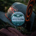 Cap with a cologne bottle labeled 'MJC' and a knife on a grassy background