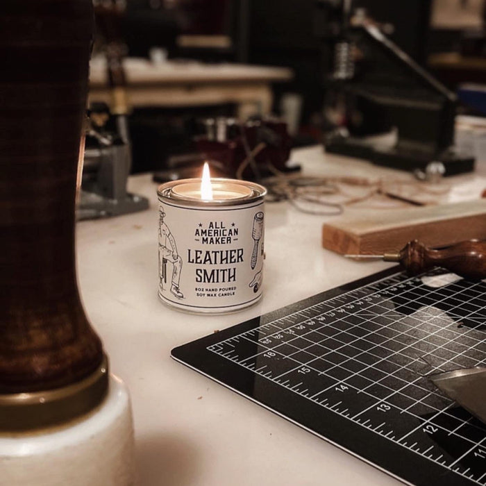 Candle labeled 'Leather Smith' on a workbench with tools and equipment in the background