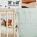 Baby crib with a textured green blanket and dimensions displayed