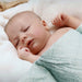 Newborn baby sleeping peacefully wrapped in a light green blanket on a soft white surface.