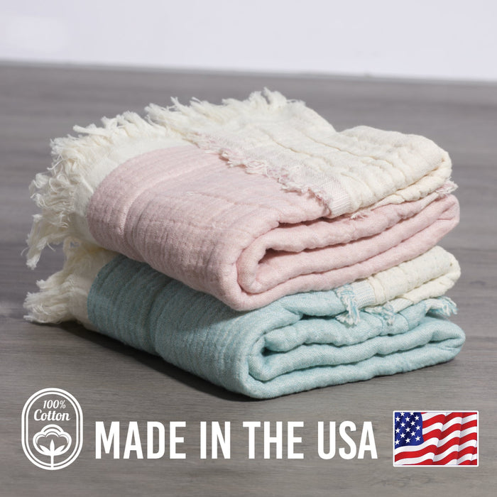 Stack of folded towels in pastel colors on a wooden surface with 'Made in the USA' and '100% Cotton' labels.