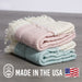 Stack of folded towels in pastel colors on a wooden surface with 'Made in the USA' and '100% Cotton' labels.