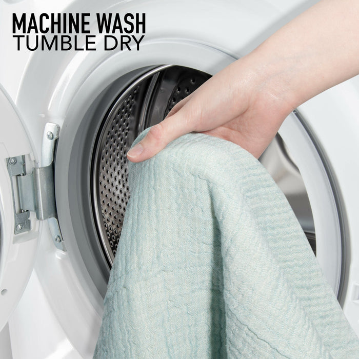 Person placing a light blue towel into a washing machine with text 'Machine Wash Tumble Dry'.