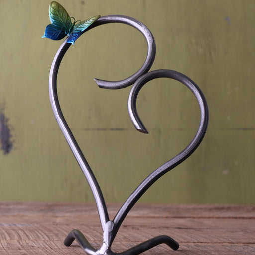 Heart-shaped metal stand with a decorative butterfly on a wooden surface and green background