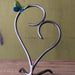 Heart-shaped metal stand with a decorative butterfly on a wooden surface and green background