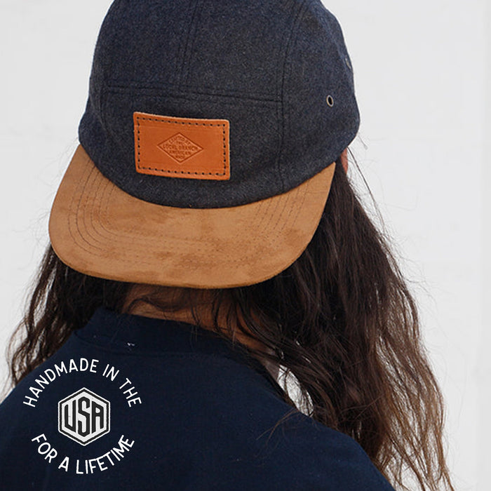 Person wearing a navy cap with brown brim and leather patch, back view.