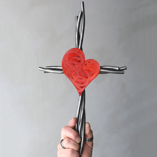 Hand holding a cross with a red heart design against a gray background