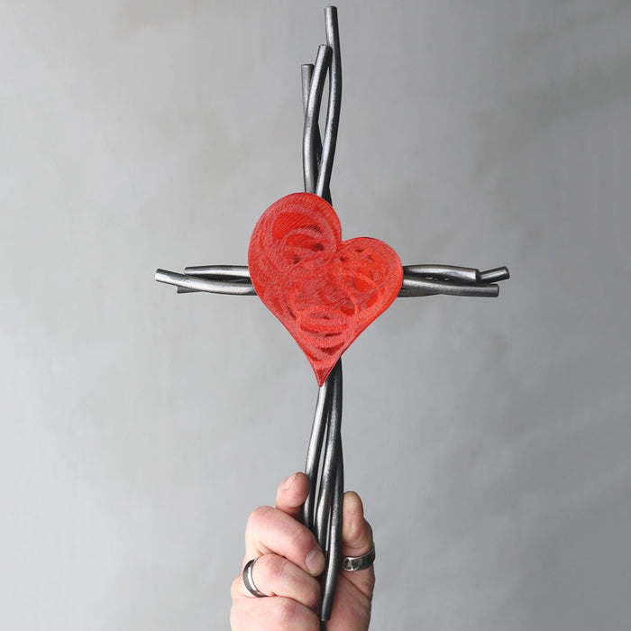 Hand holding a cross with a red heart design against a gray background