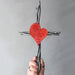 Hand holding a cross with a red heart design against a gray background