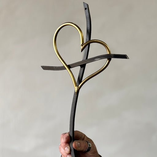 Hand holding a decorative item with interlocking hearts made of black and gold metal against a plain background