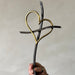 Hand holding a decorative item with interlocking hearts made of black and gold metal against a plain background