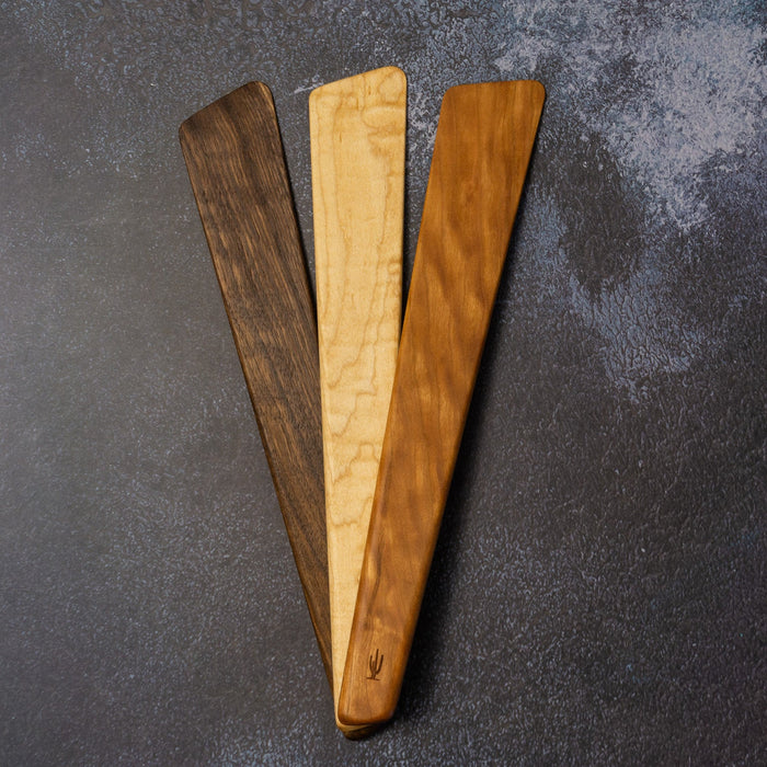 Three wooden spatulas on a dark textured surface