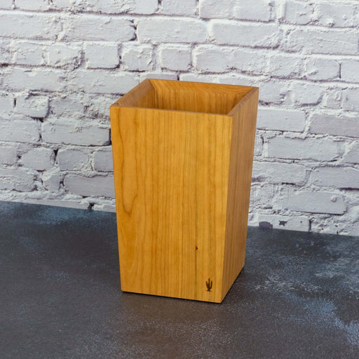 Wooden utensil-holder against a white brick wall.