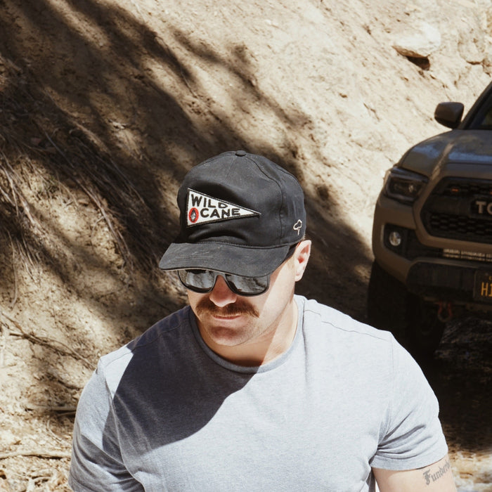 Man wearing a cap and sunglasses in front of a off-road vehicle on a dirt road.