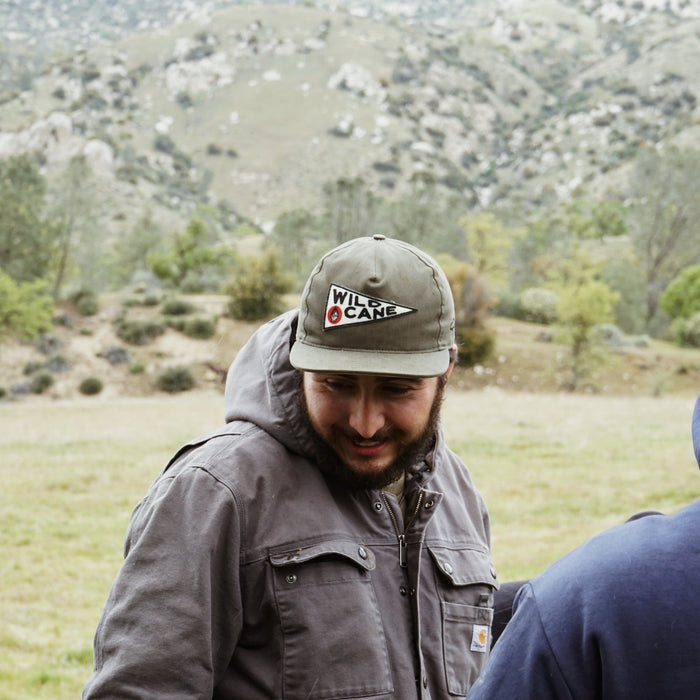 Man wearing a cap and jacket in a field with mountains in the background