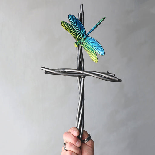 Hand holding a metal dragonfly sculpture against a gray background
