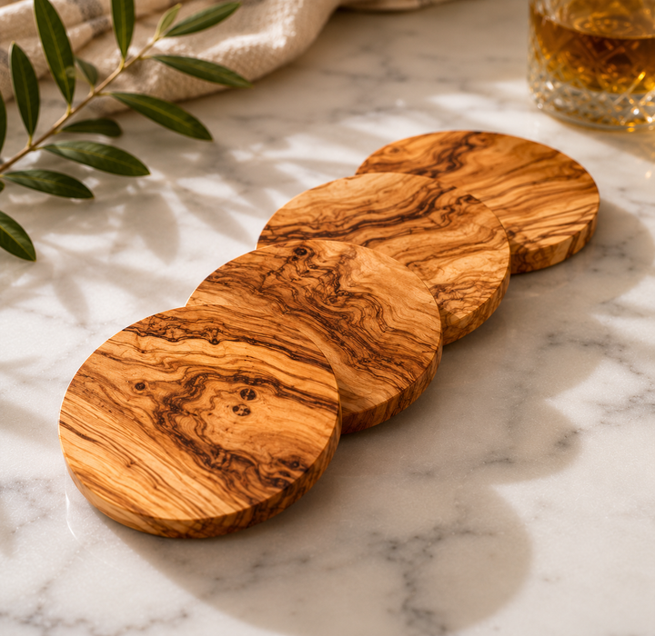 Set of wooden coasters on a marble surface with a glass of whiskey and olive branch.