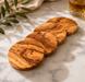 Set of wooden coasters on a marble surface with a glass of whiskey and olive branch.