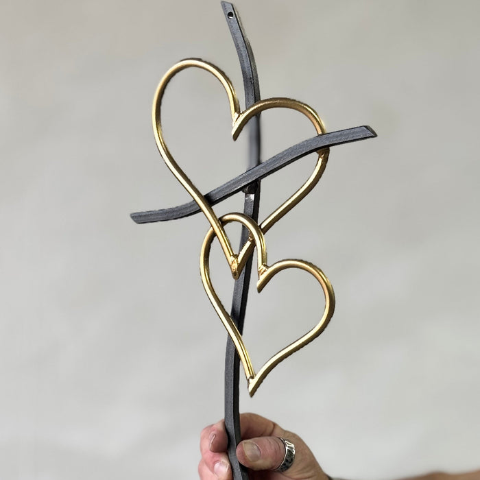 Decorative metal heart sculpture held by a hand against a plain background