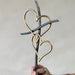 Decorative metal heart sculpture held by a hand against a plain background