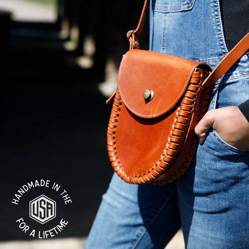 Person wearing a brown leather bag with 'Handmade in the USA for a Lifetime' logo.
