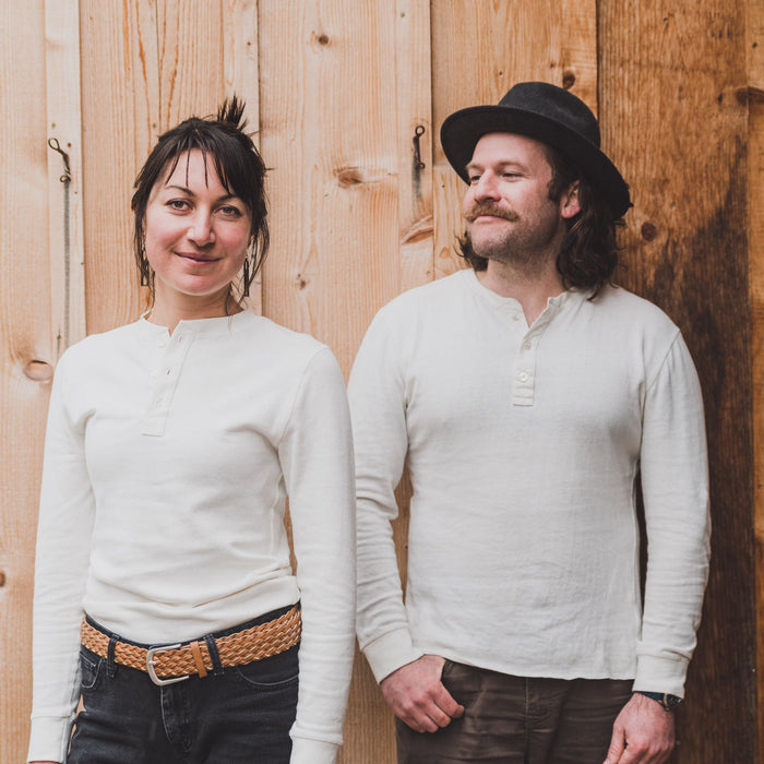 Two people wearing white shirts standing against a wooden wall.