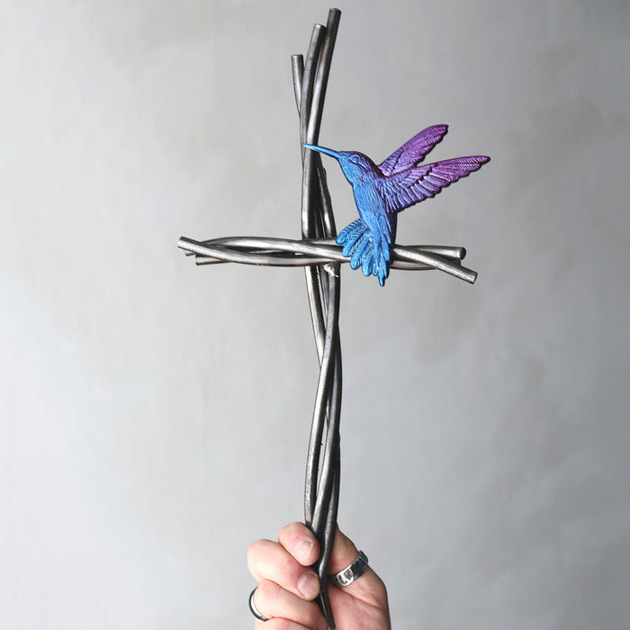 Hand holding a cross-shaped object with a blue bird figure against a plain background
