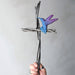 Hand holding a cross-shaped object with a blue bird figure against a plain background