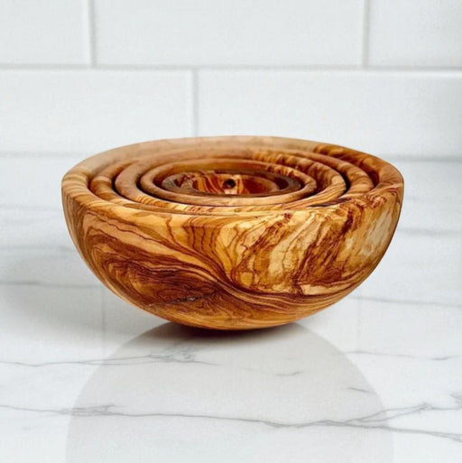 Wooden bowl with concentric designs on a marble surface with a white tiled wall background