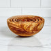 Wooden bowl with concentric designs on a marble surface with a white tiled wall background