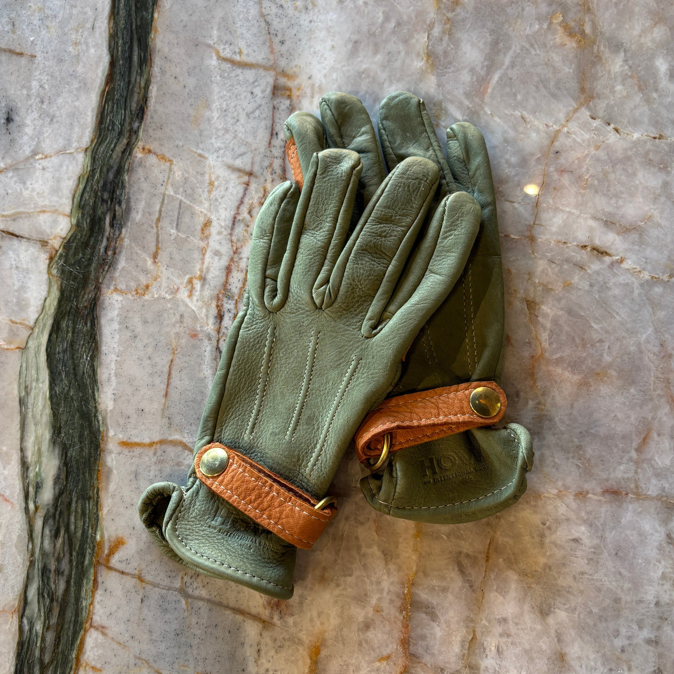 Pair of green leather gloves with brown accents on a marble surface