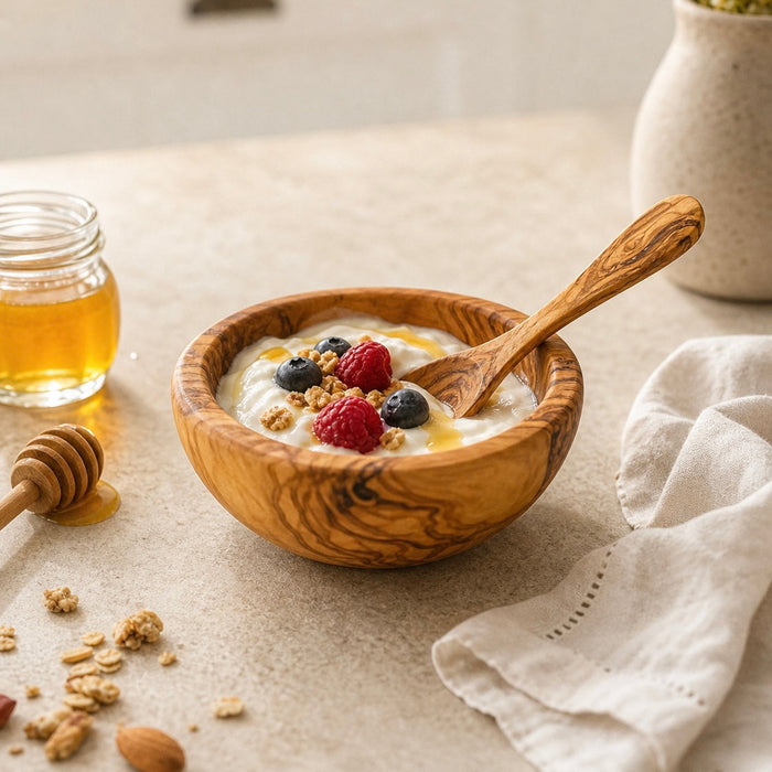 Wooden bowl with yogurt, berries, and granola on a light surface with honey and a towel.